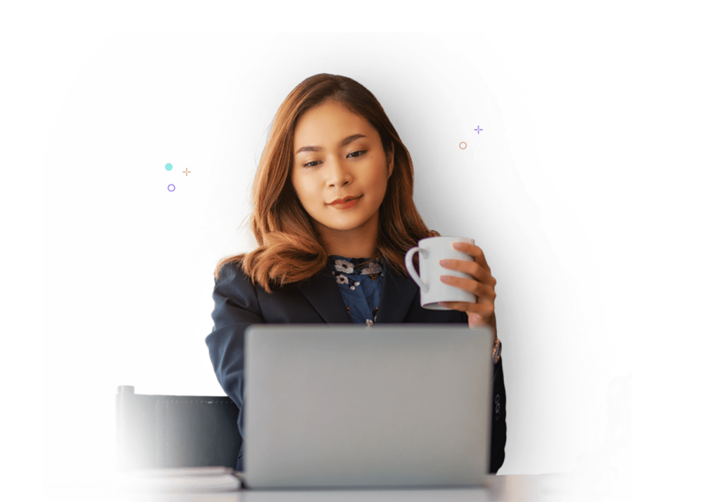 A woman holding a white cup of coffee while working on her laptop.