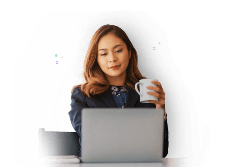 A woman holding a white cup of coffee while working on her laptop.