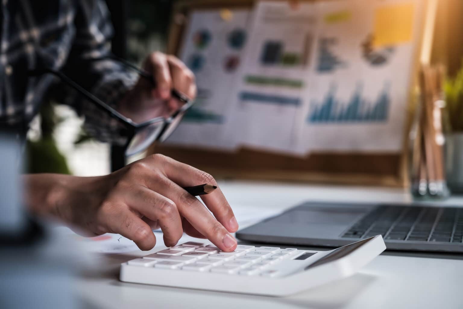 Man using calculator at desk in front of laptop with graphs in the background