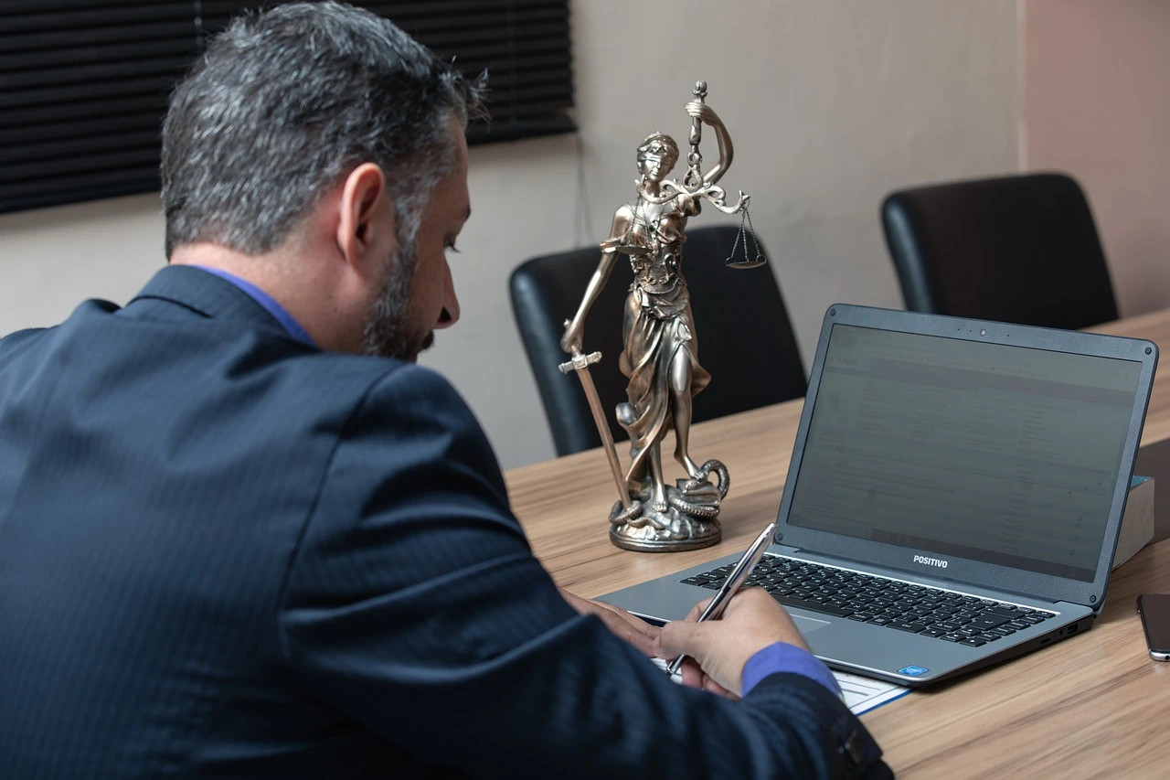 A lawyer working on his laptop with a small figurine of Lady Justice in front of him.