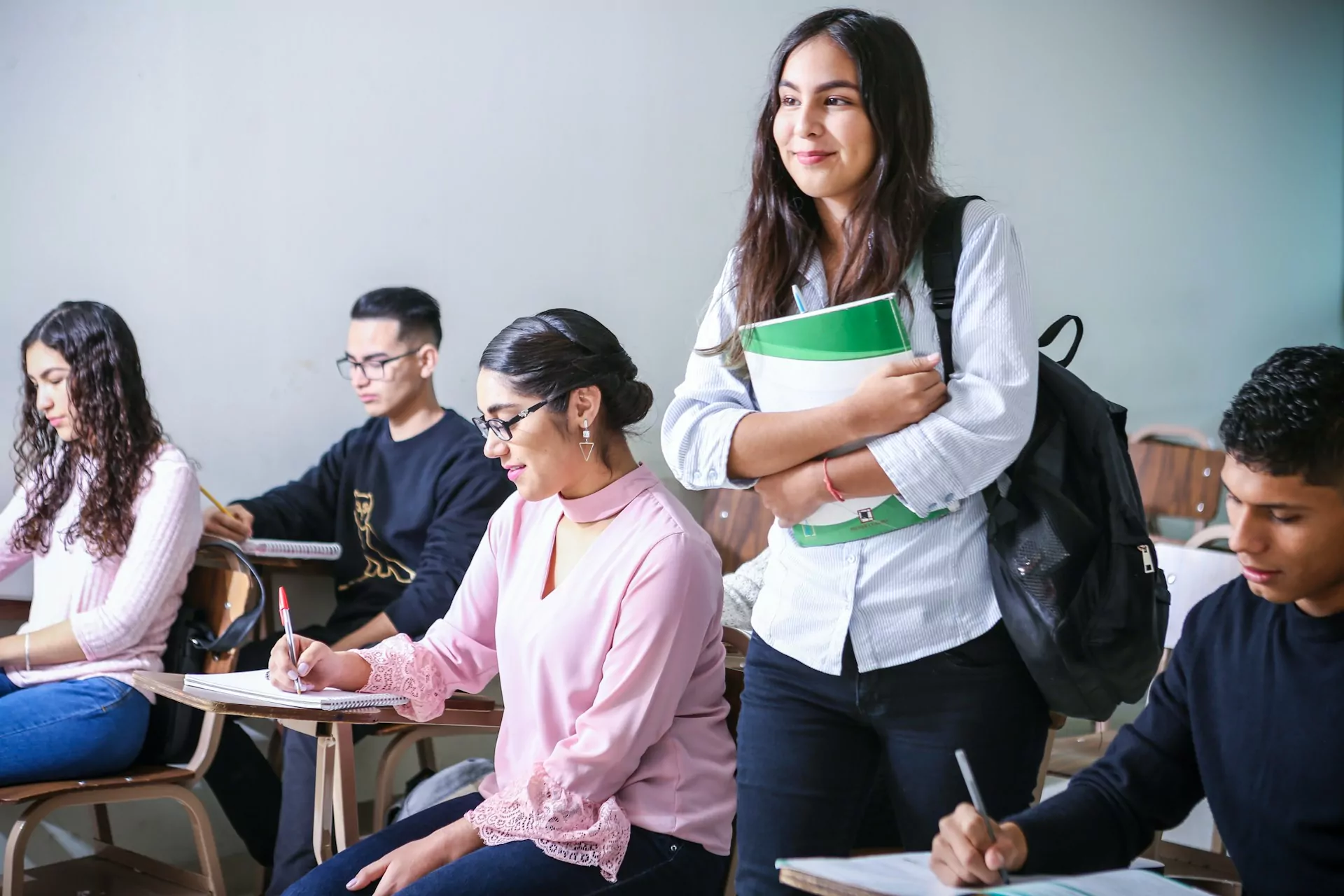 A girl carrying a green notebook in the classroom.