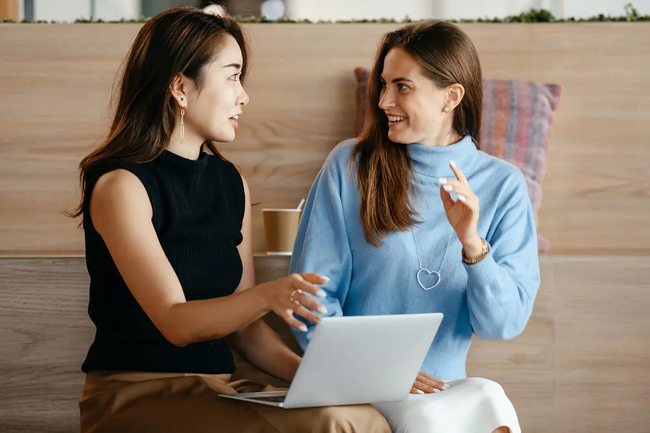 Two women with a laptop discussing time tracking practices.