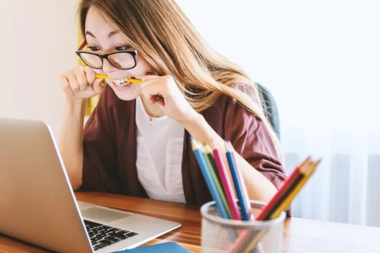 A frustrated Asian woman in an office setting bites her pencil while staring at a laptop by Jeshoots Com on Unsplash.