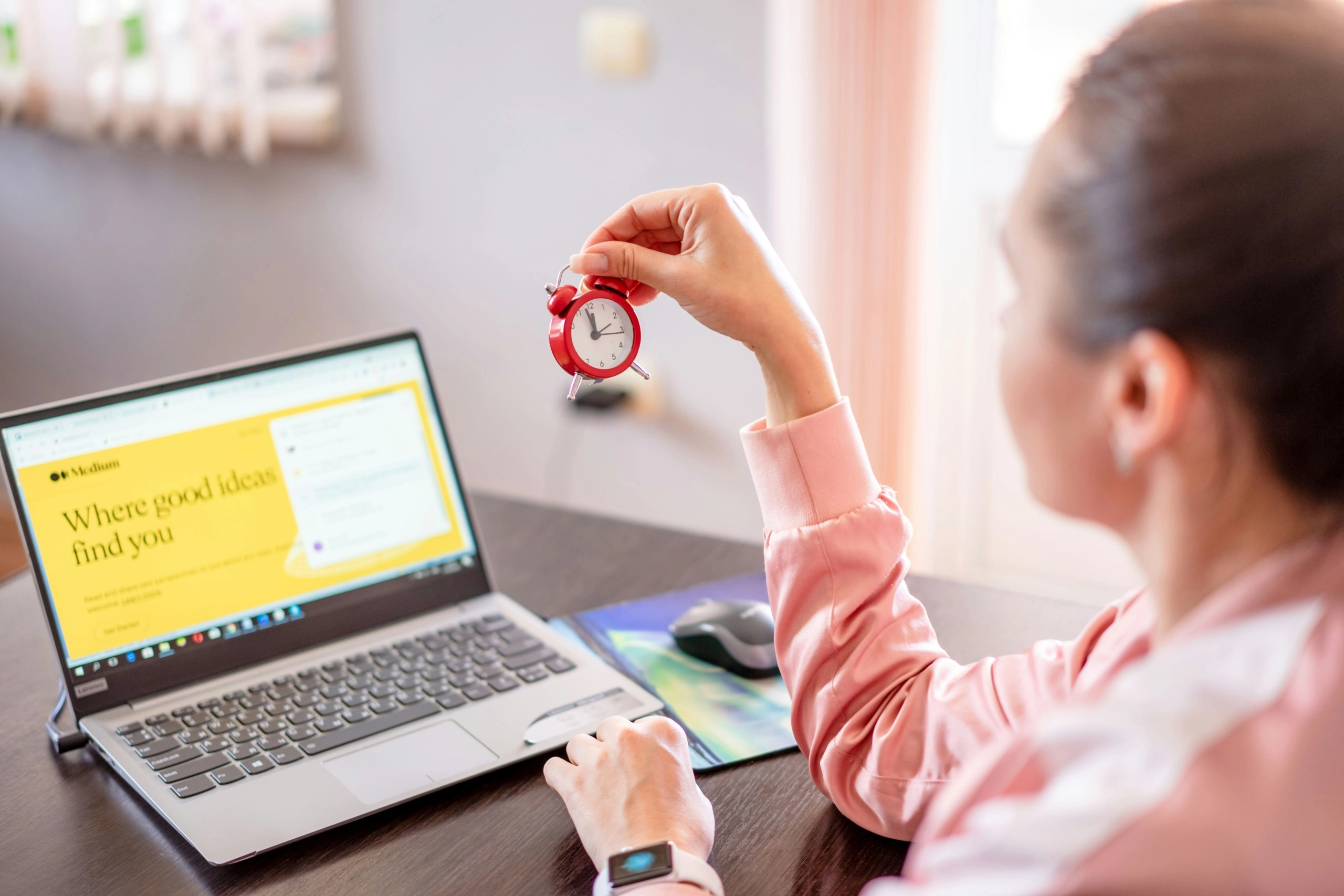 Eine Frau, die an einem Laptop arbeitet und auf eine Uhr schaut