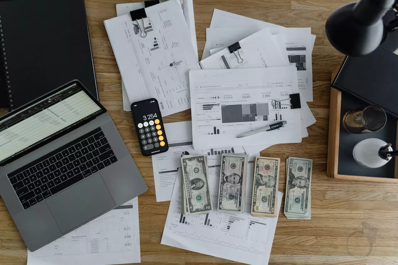 Revenue leakage analysis. A table with a laptop, a bunch of financial paperwork, and cash on top. Photo by Tima Miroshnichenko