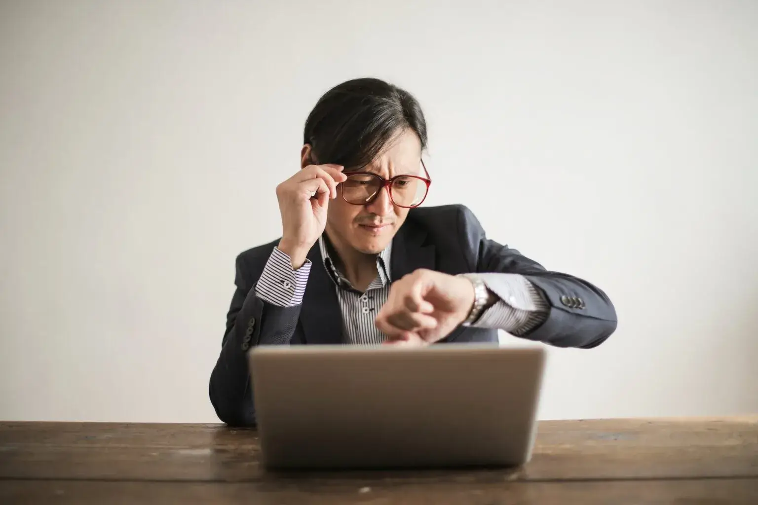 Un hombre vestido con traje y gafas mirando la hora en su reloj.