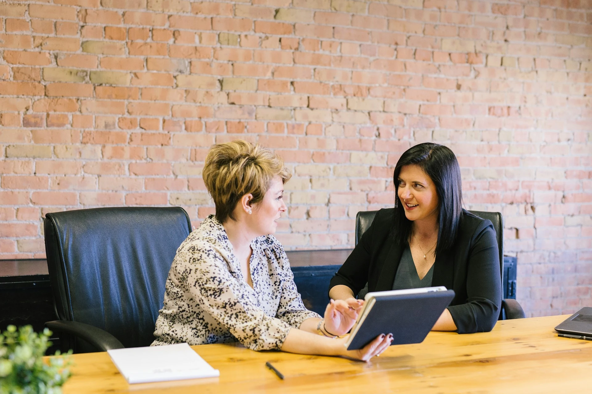 Two women discussing something, the other one holding up a notebook.