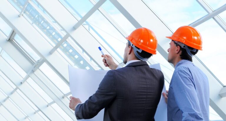 Two men with blueprints inspecting structure