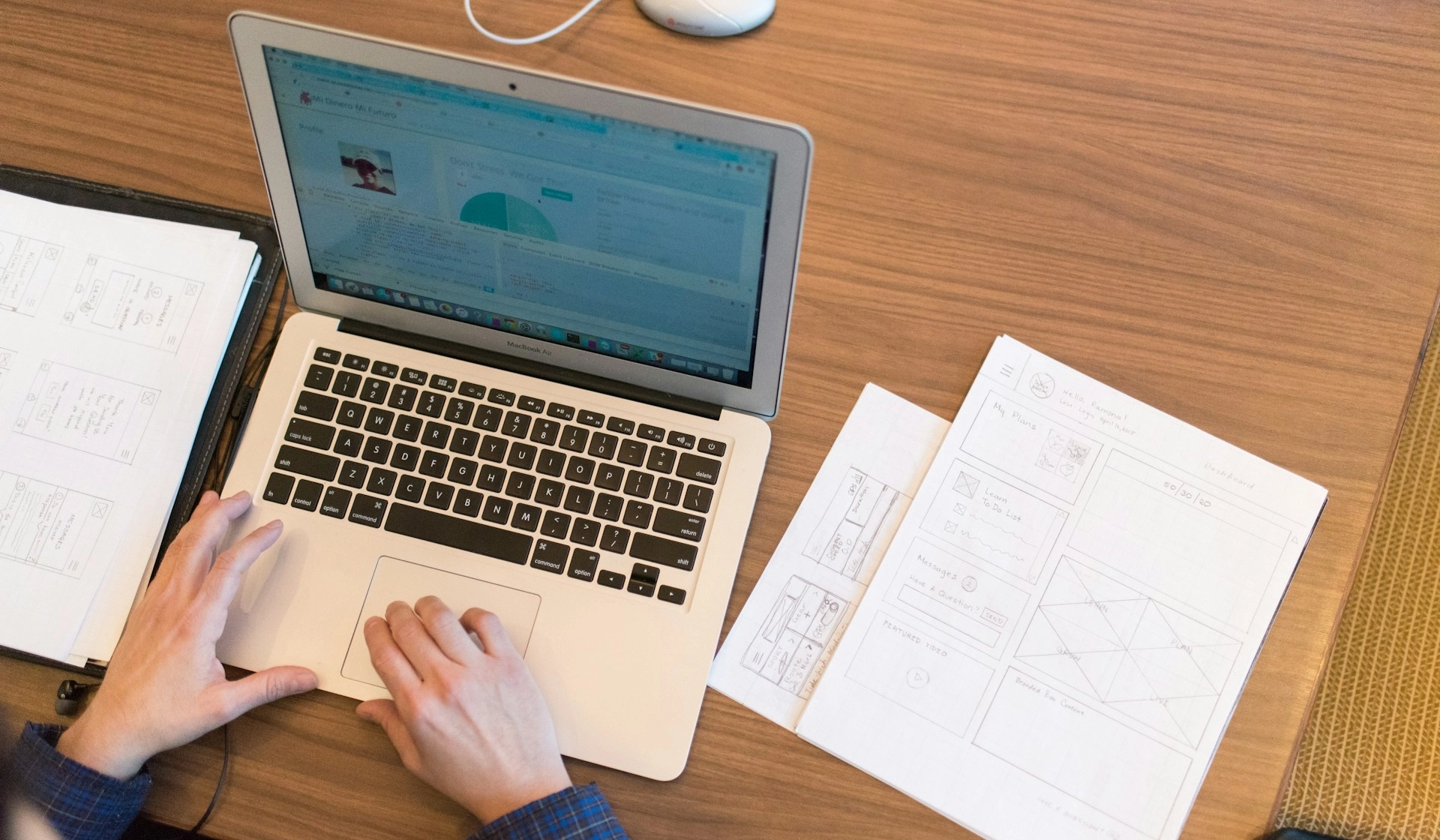 A personworking on a laptop in a table with paperwork next to the laptop.