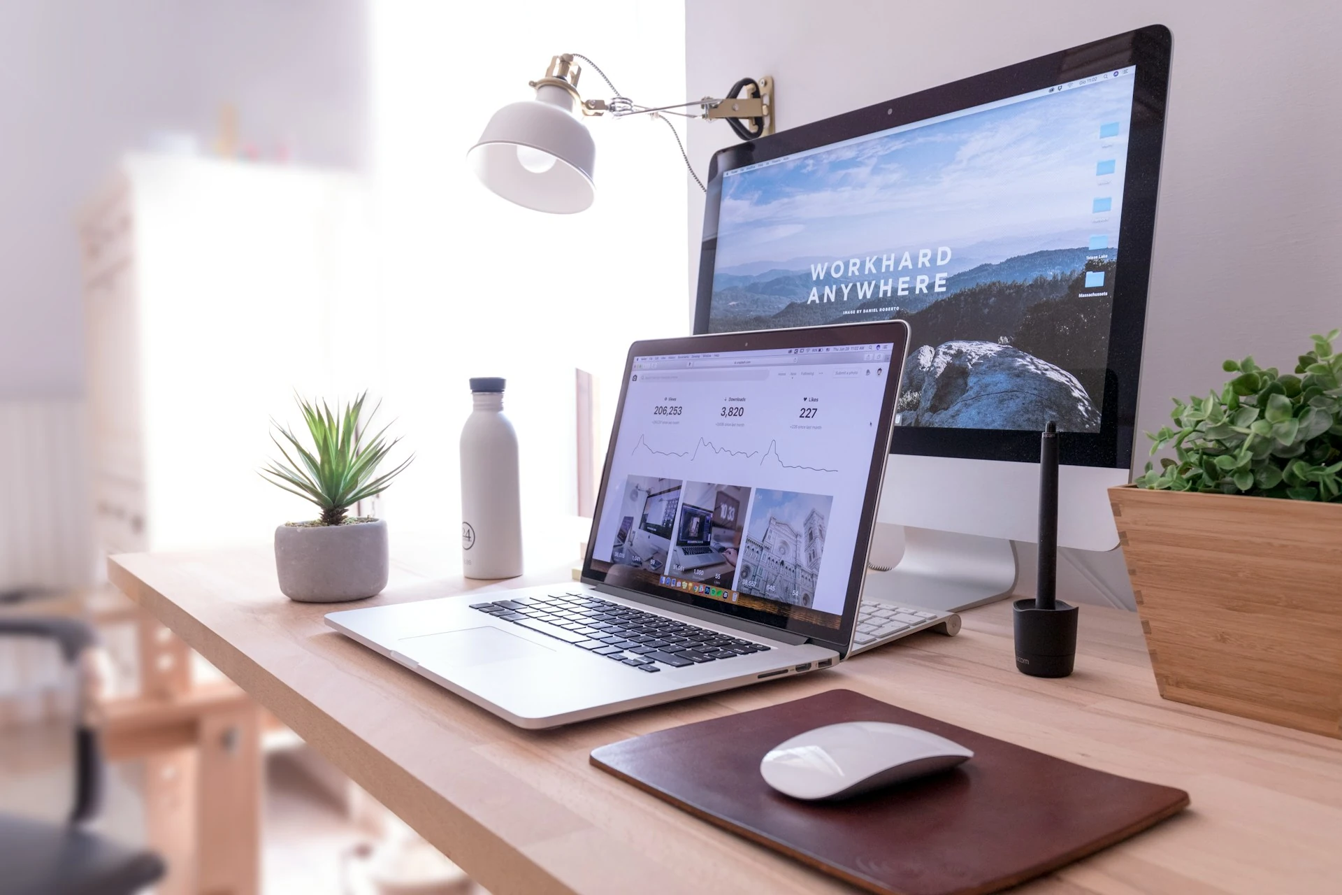A MacBook Pro sits on a table beside a white iMac and Magic Mouse.
