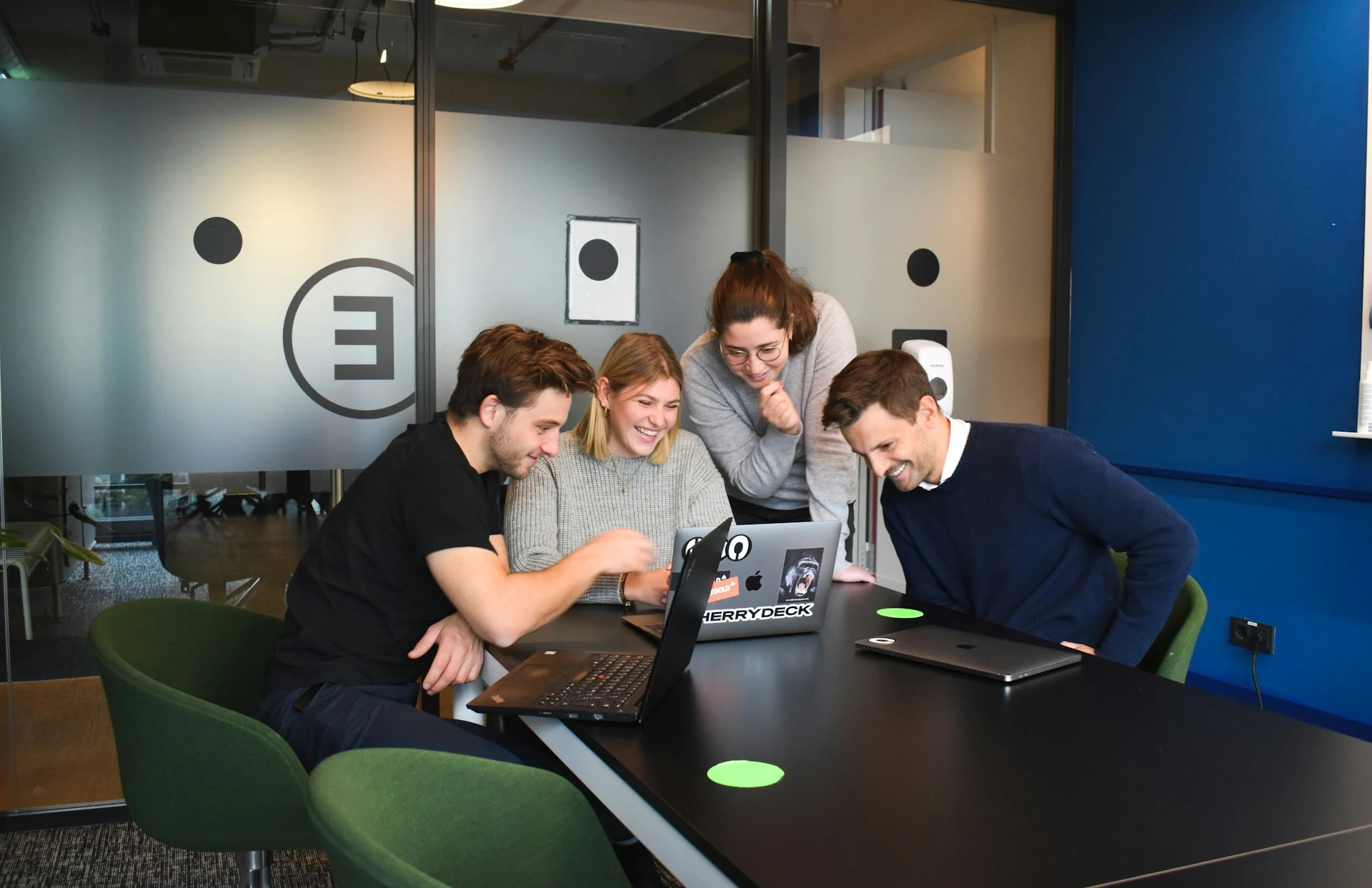 People sitting on chairs in front of laptop computers, smiling and discussing something for work.