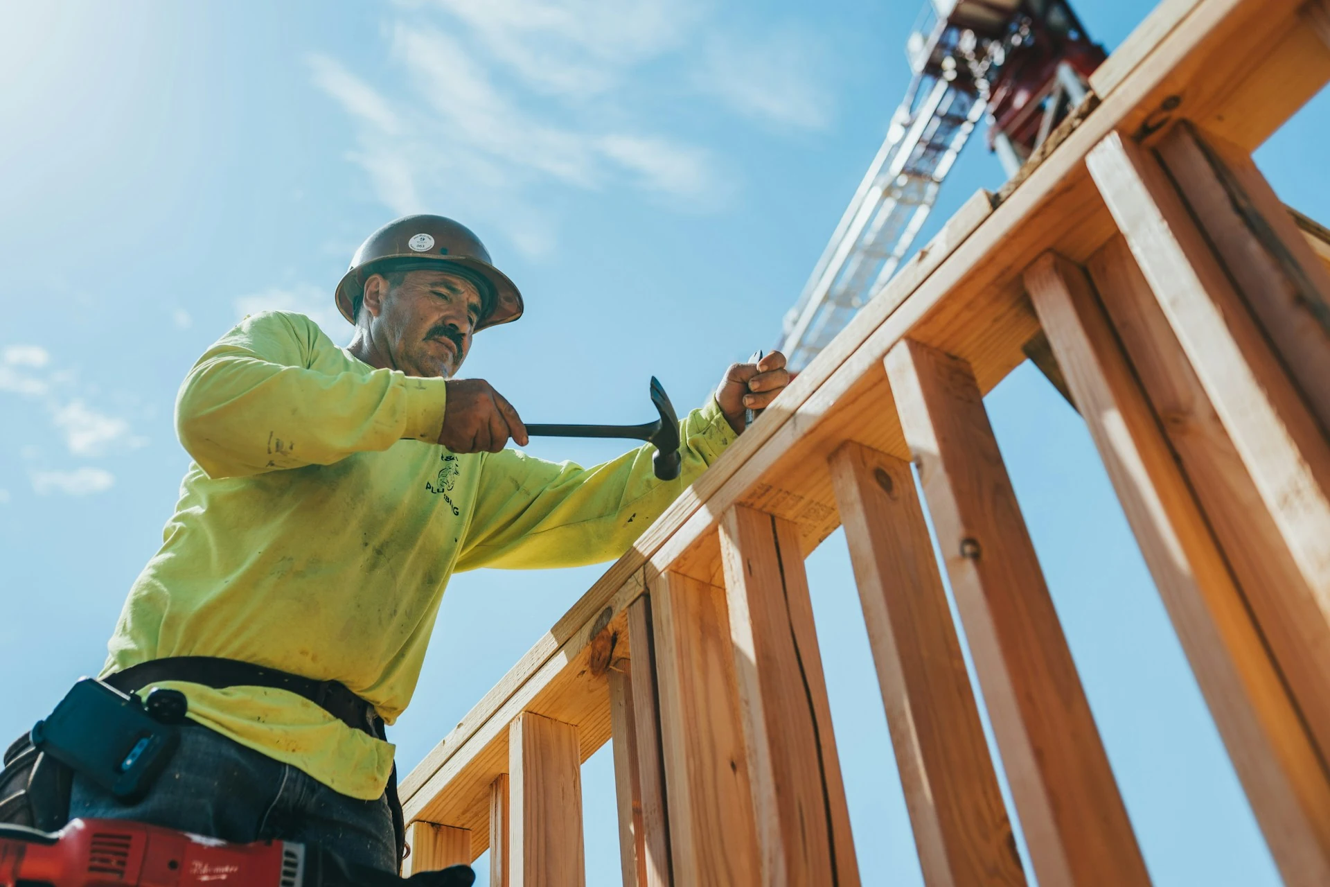 A man in a hard hat and safety gear works on a wooden structure.