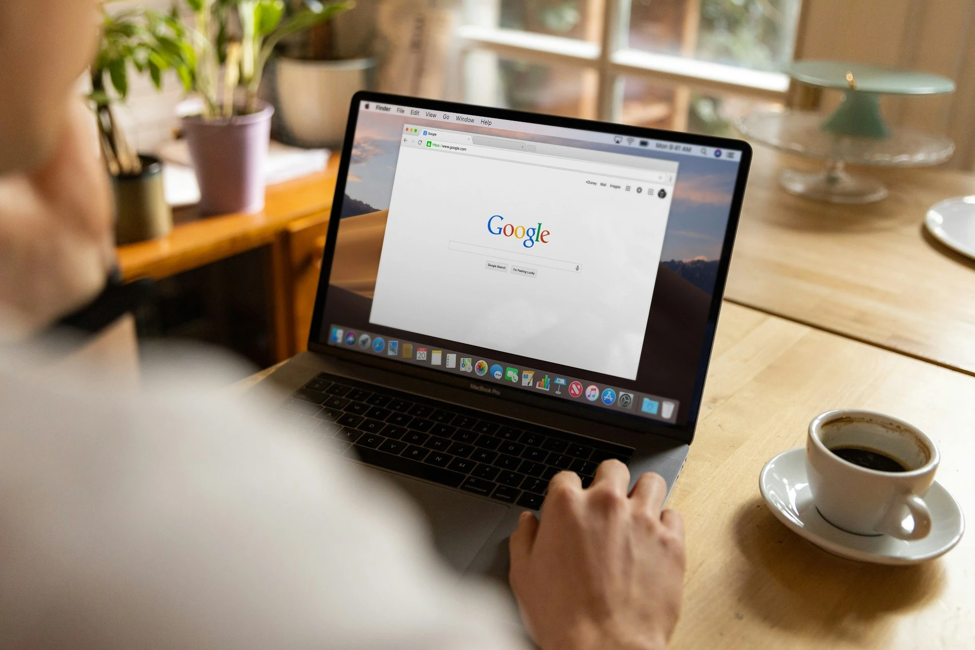 A person uses a MacBook Pro on a table with the Google home page displayed on screen.