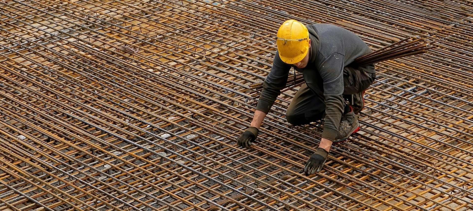 A man in a black jacket and yellow helmet in a construction site.