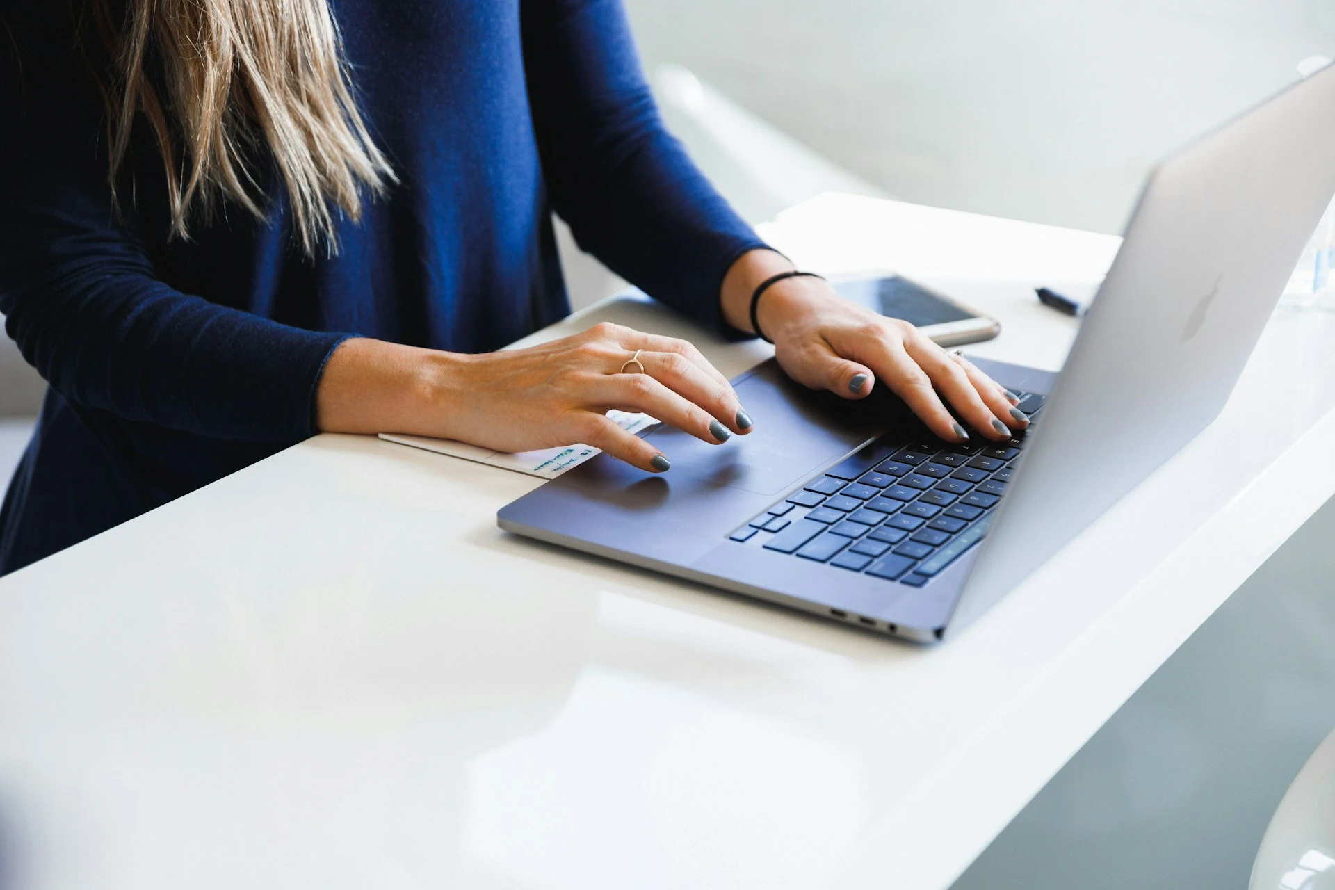 A woman in blue long sleeves working on her laptop.