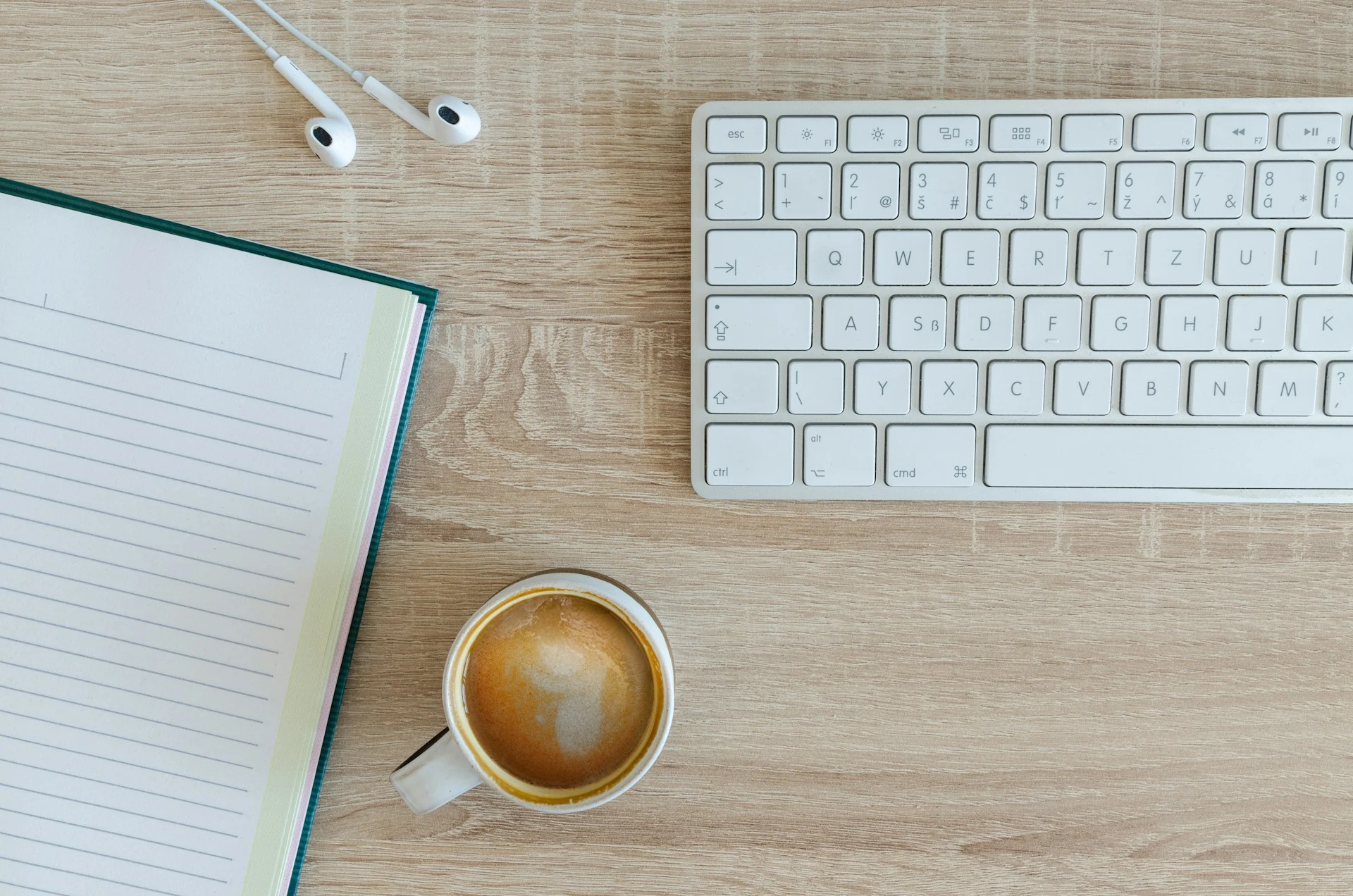 A keyboard, notebook, wired headphones, and a cup of coffee.
