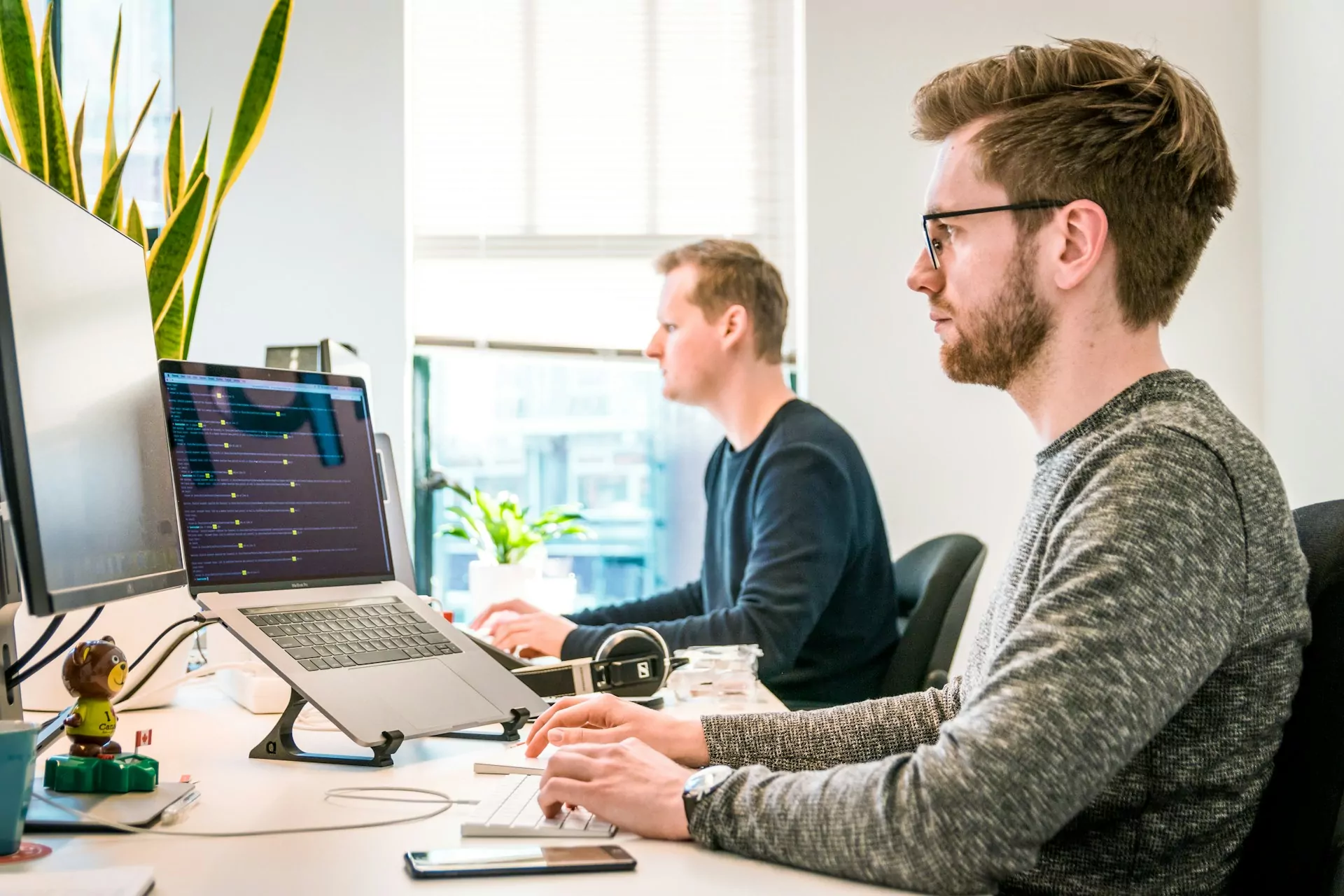 Two guys sitting side by side while working on their laptops.