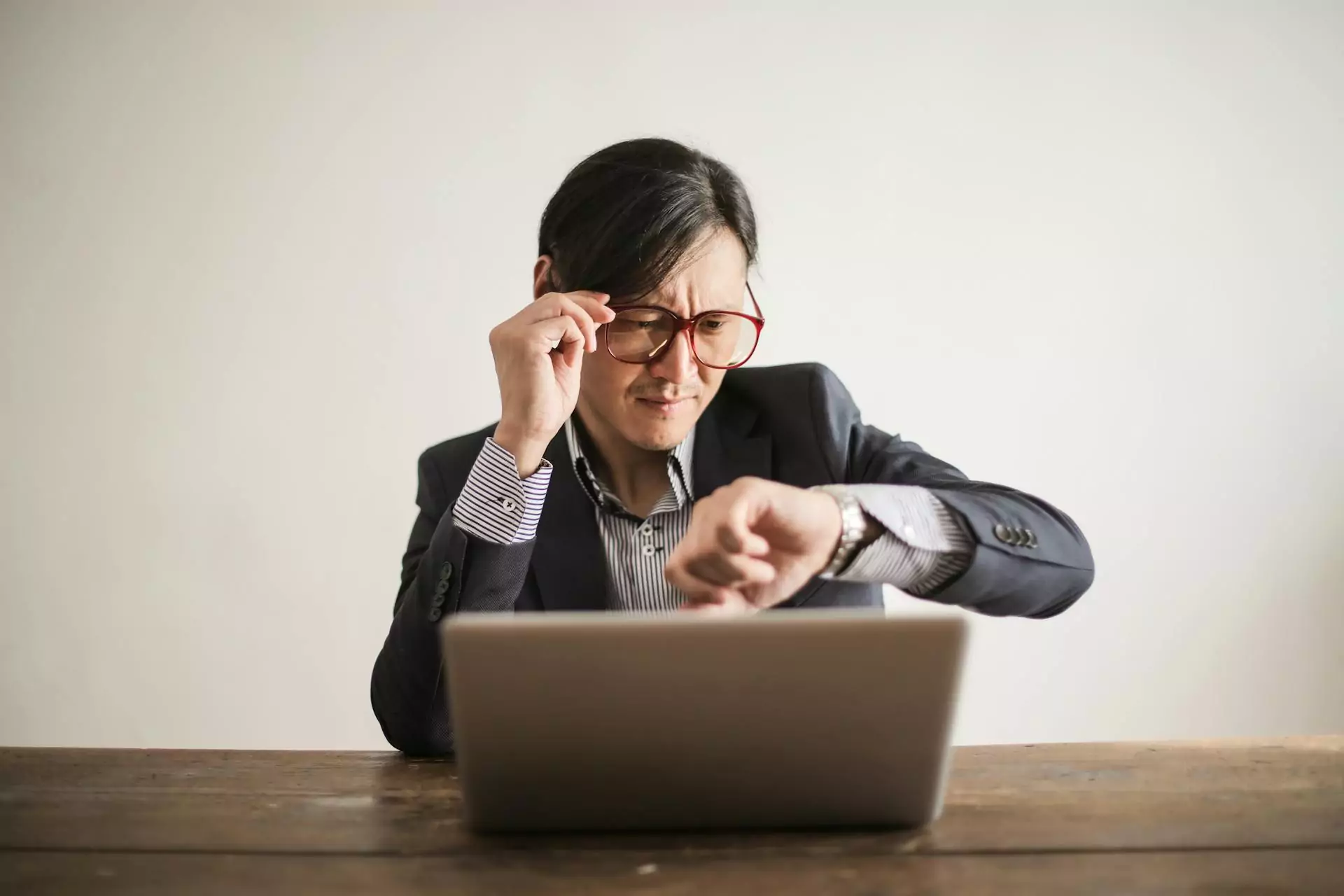 Homem conferindo a hora em seu relógio enquanto trabalha no notebook.