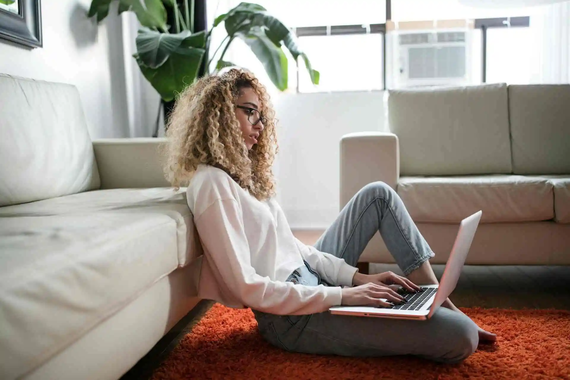 Uma mulher trabalhando em seu notebook sentada no chão de sua sala de estar