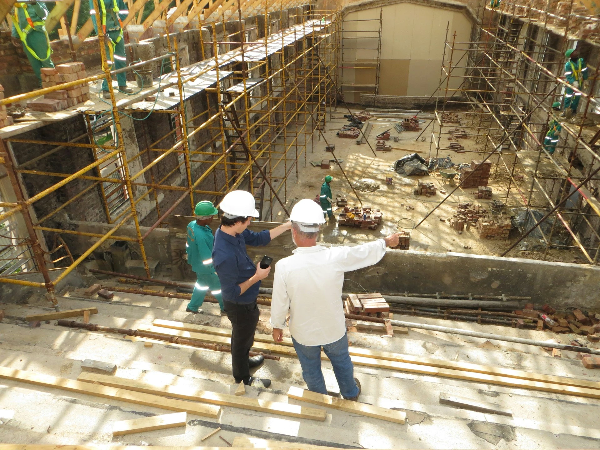 Two men in white hard hats pointing at a construction site.