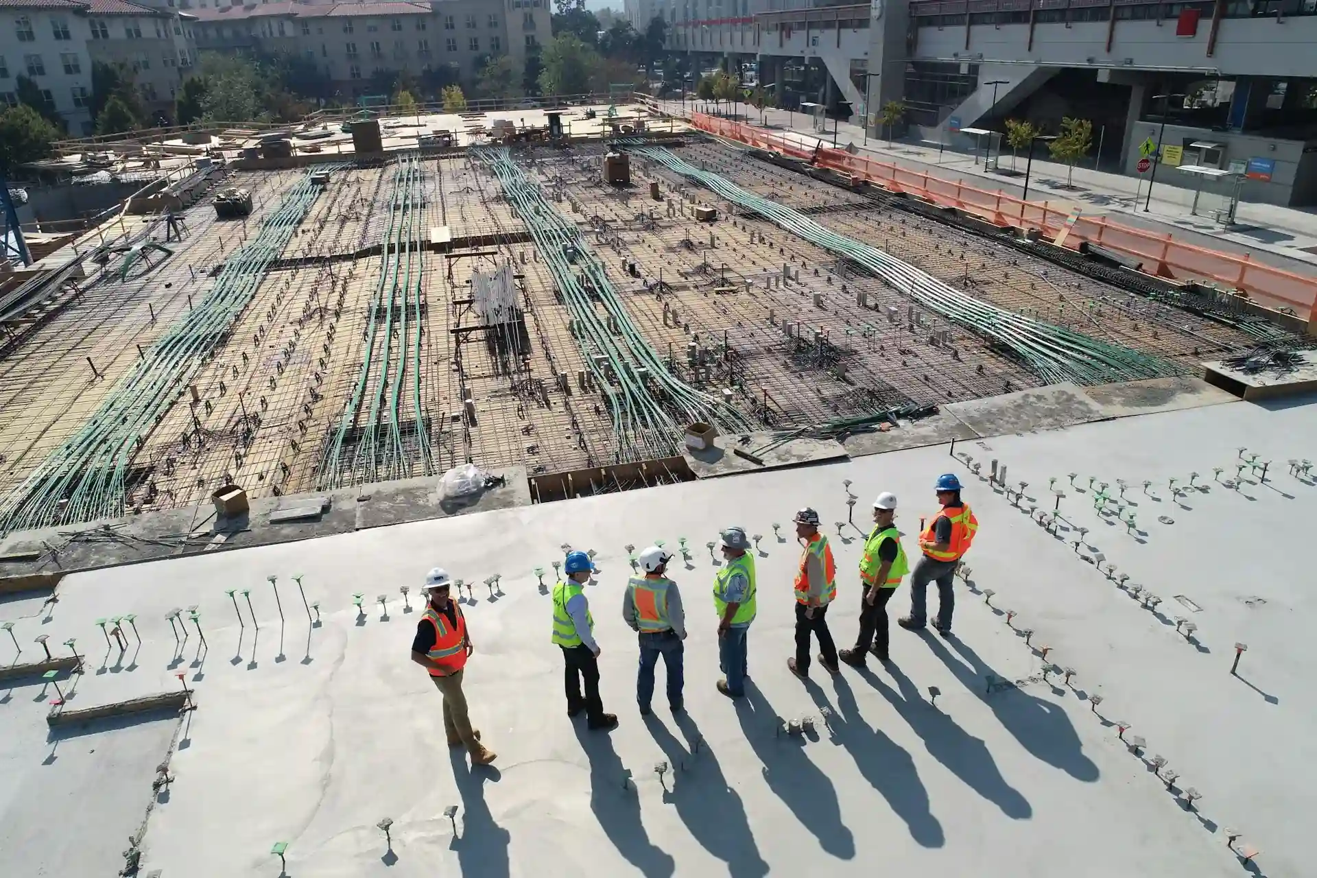 A team of engineers and construction workers in safety gear inspecting a large construction site with reinforced concrete and exposed rebar.