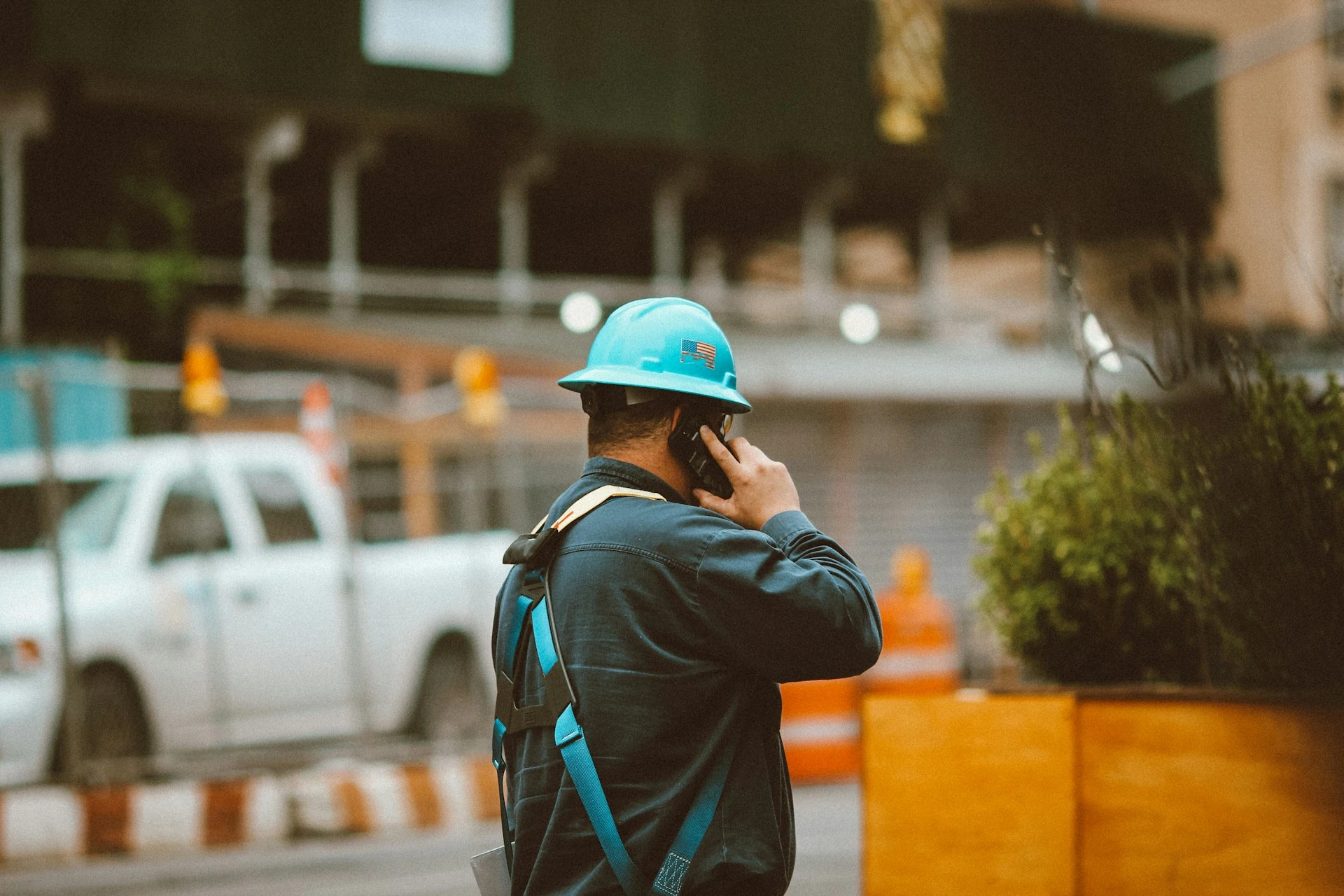 A man in a blue jacket wearing an orange helmet uses his phone to make a call.