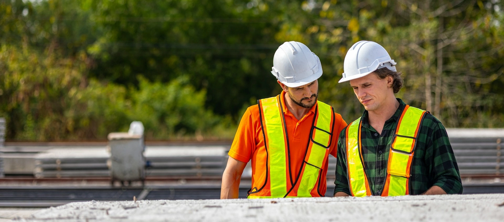 Two construction workers wearing white hard hats, talking to each other.