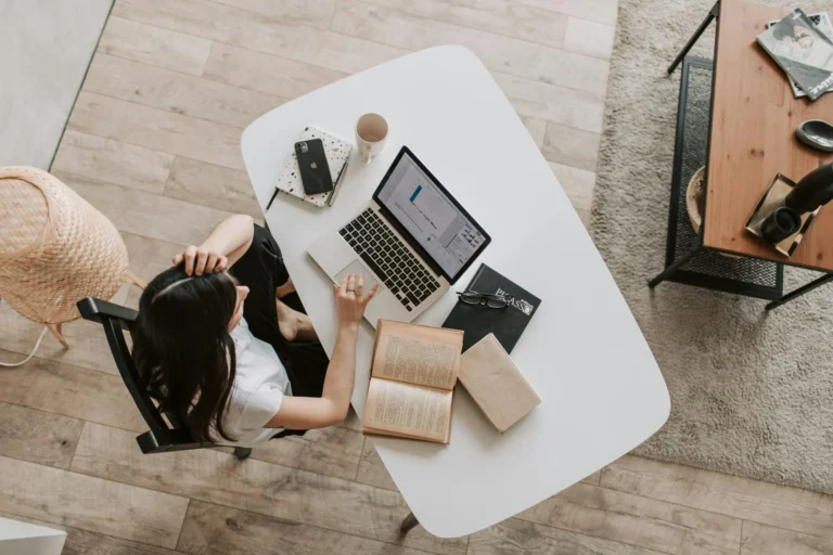 Ragazza che lavora al suo portatile con dei libri aperti sulla scrivania