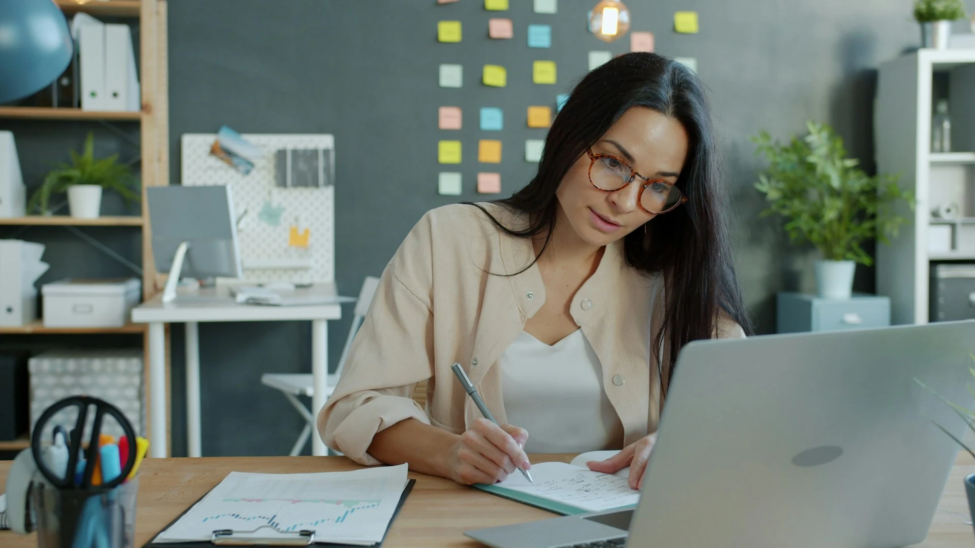 A woman works at a desk with a laptop and notebook.