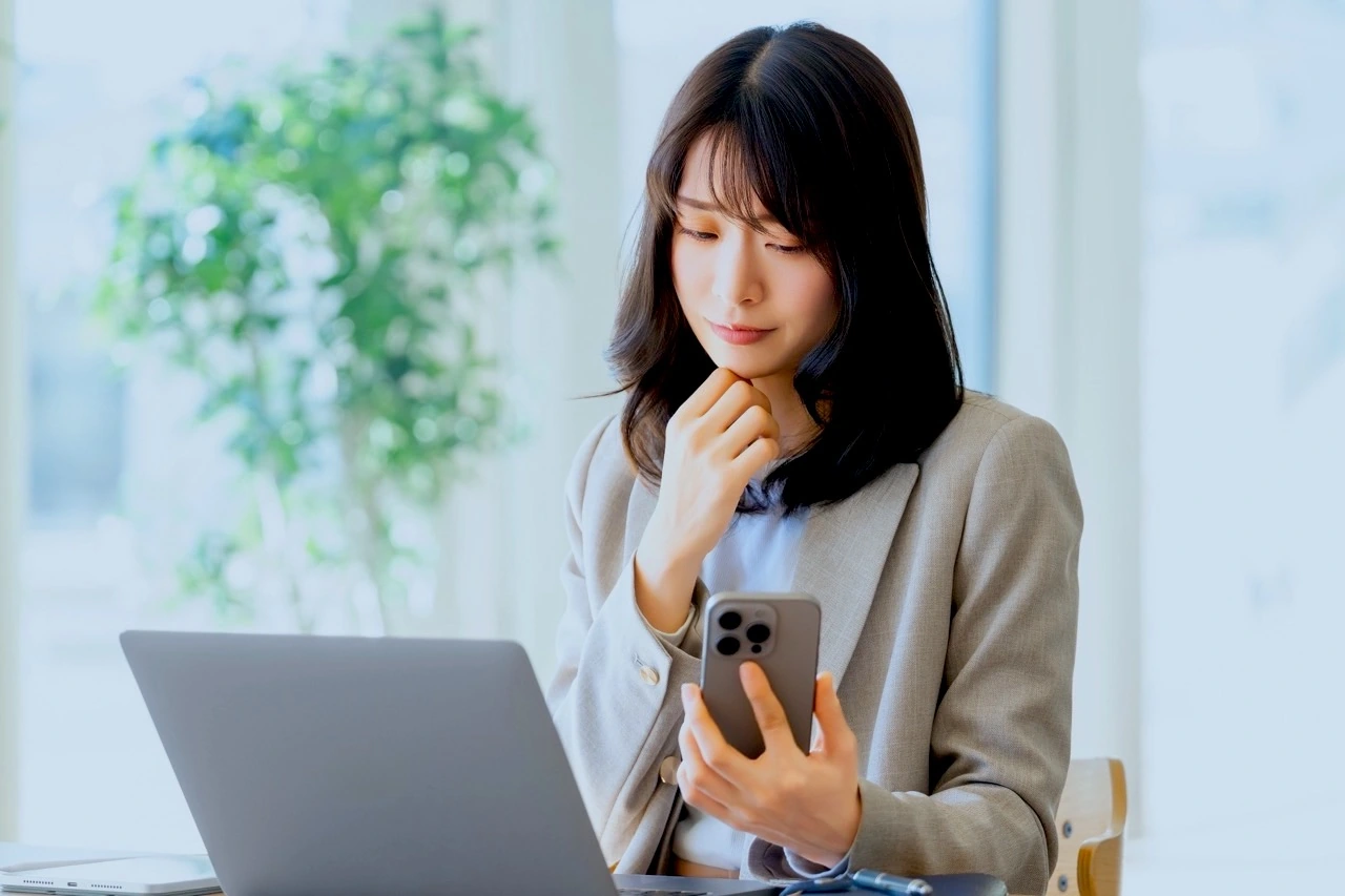 仕事中にスマホを手にして考える女性。