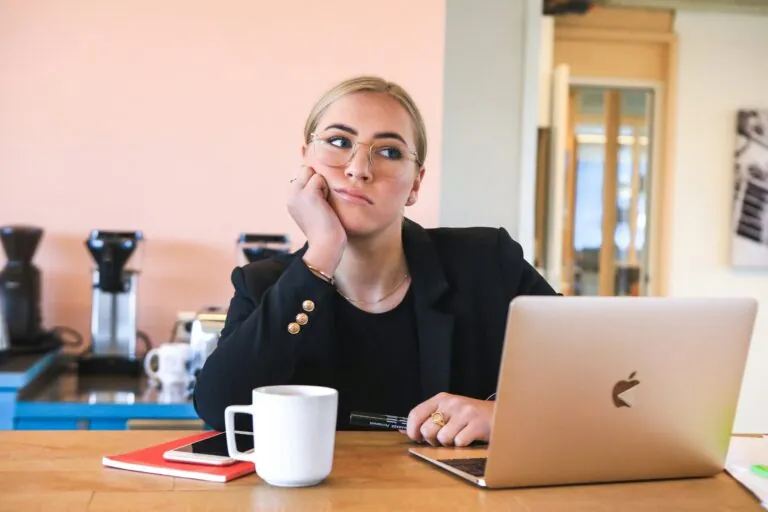 Woman at desk with laptop at coffee cup looking unfocused