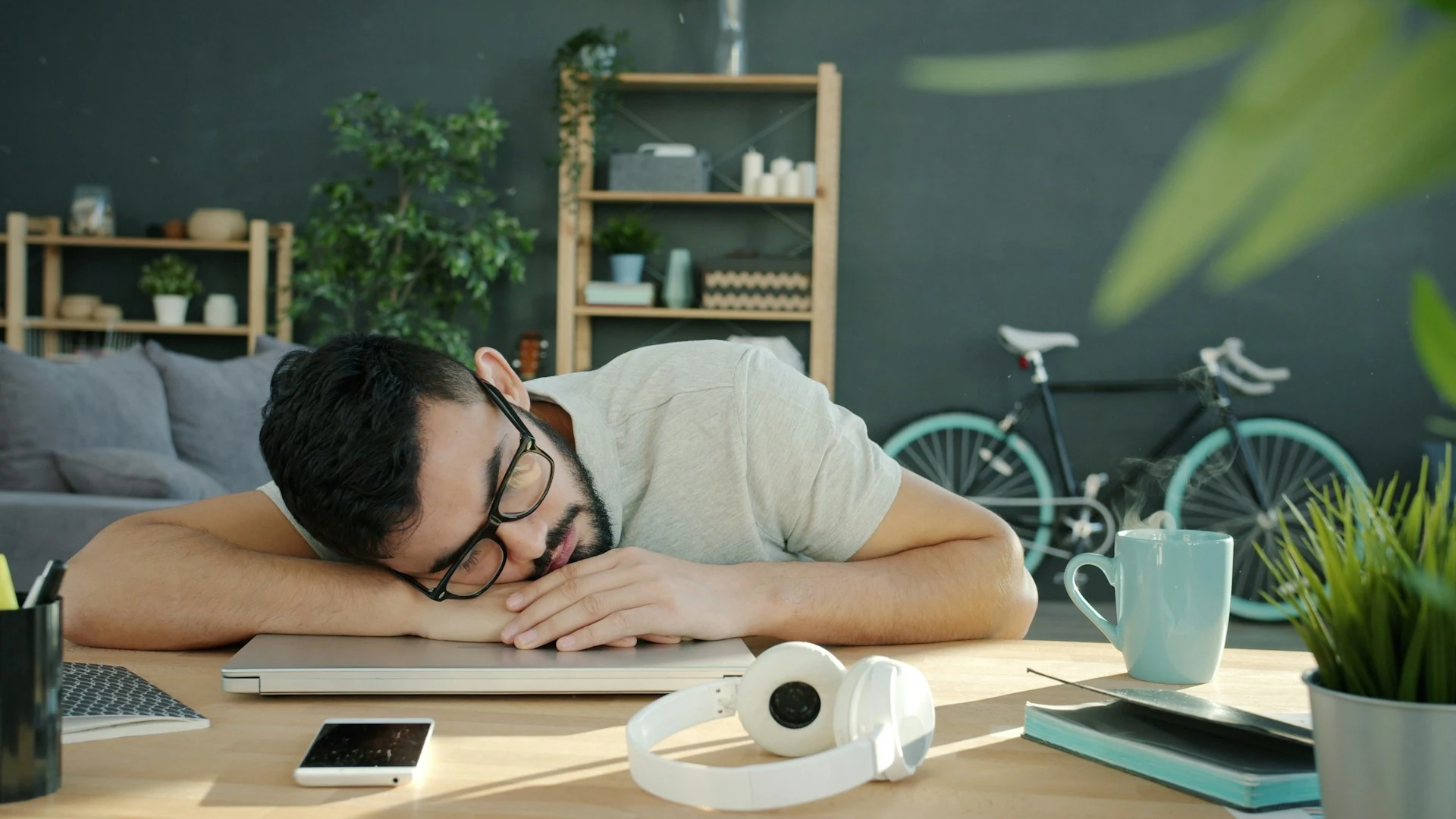 A man sleeps on a laptop at a desk.