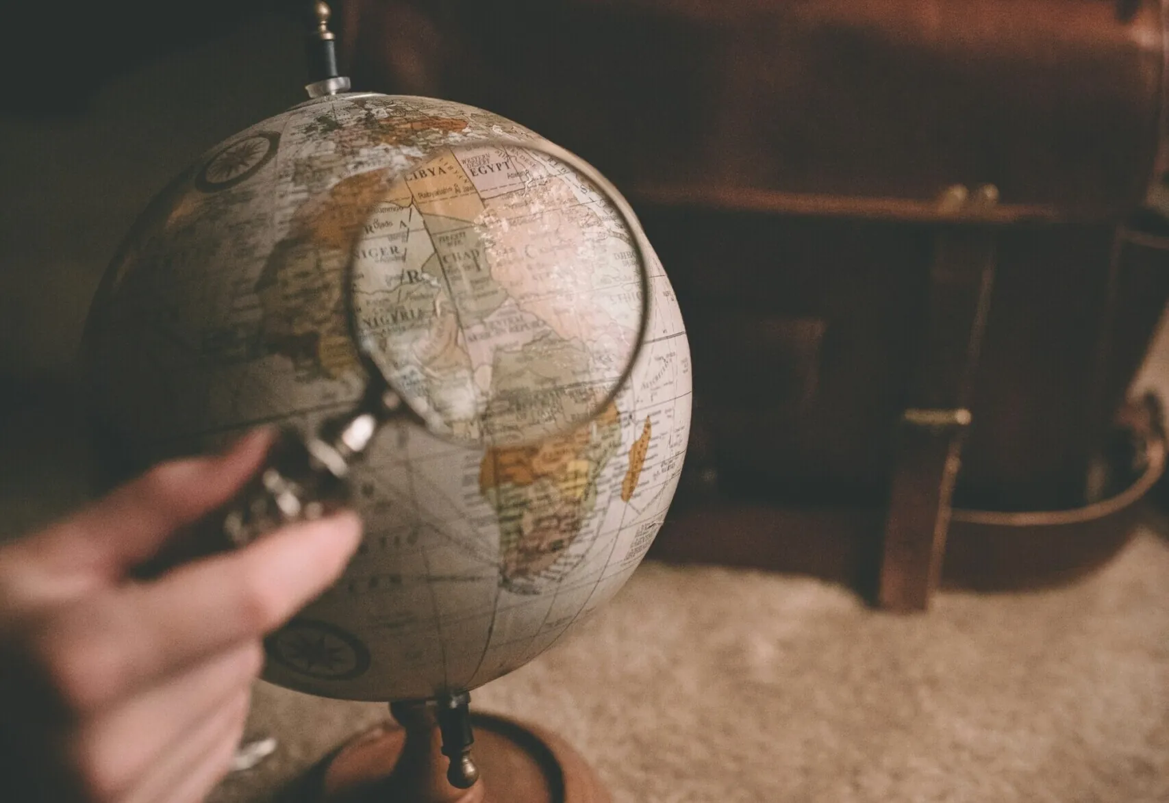 A hand holding a magnifying glass over a work globe.