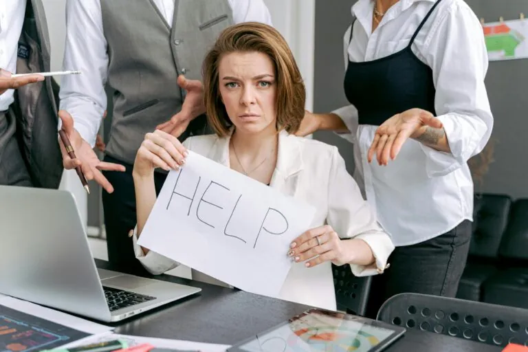 Lavoratrice in ufficio con in mano un cartello con la scritta "HELP"