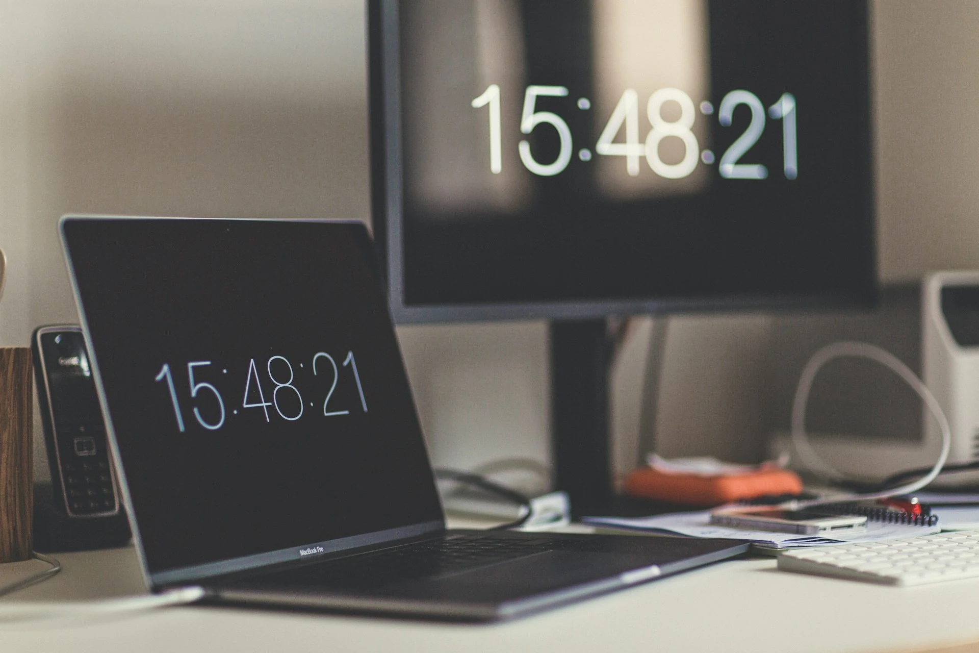 A desktop monitor and a laptop showing the time.