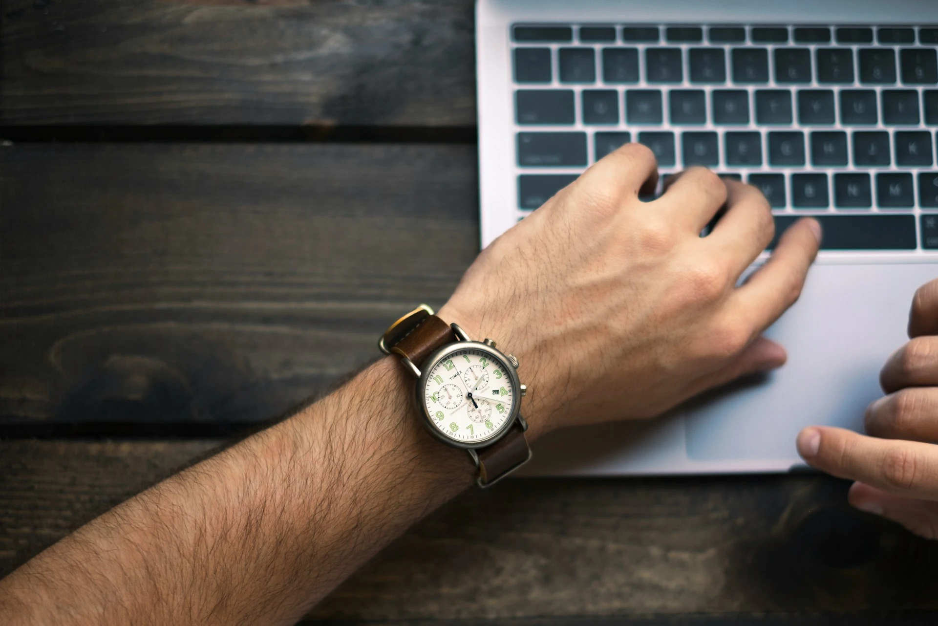 A hand with a wristwatch working on a laptop.