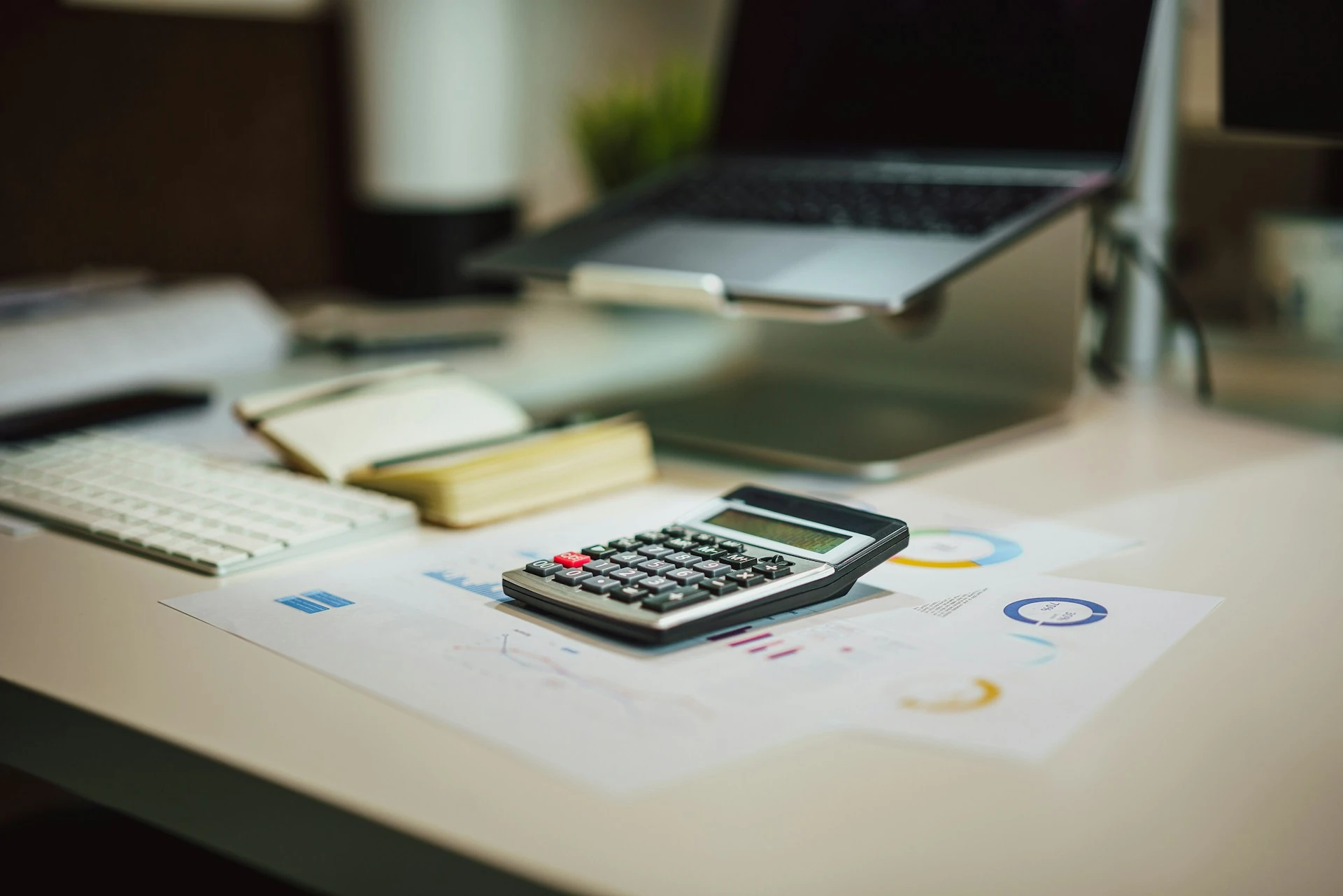 A calculator sits on a table next to a laptop.
