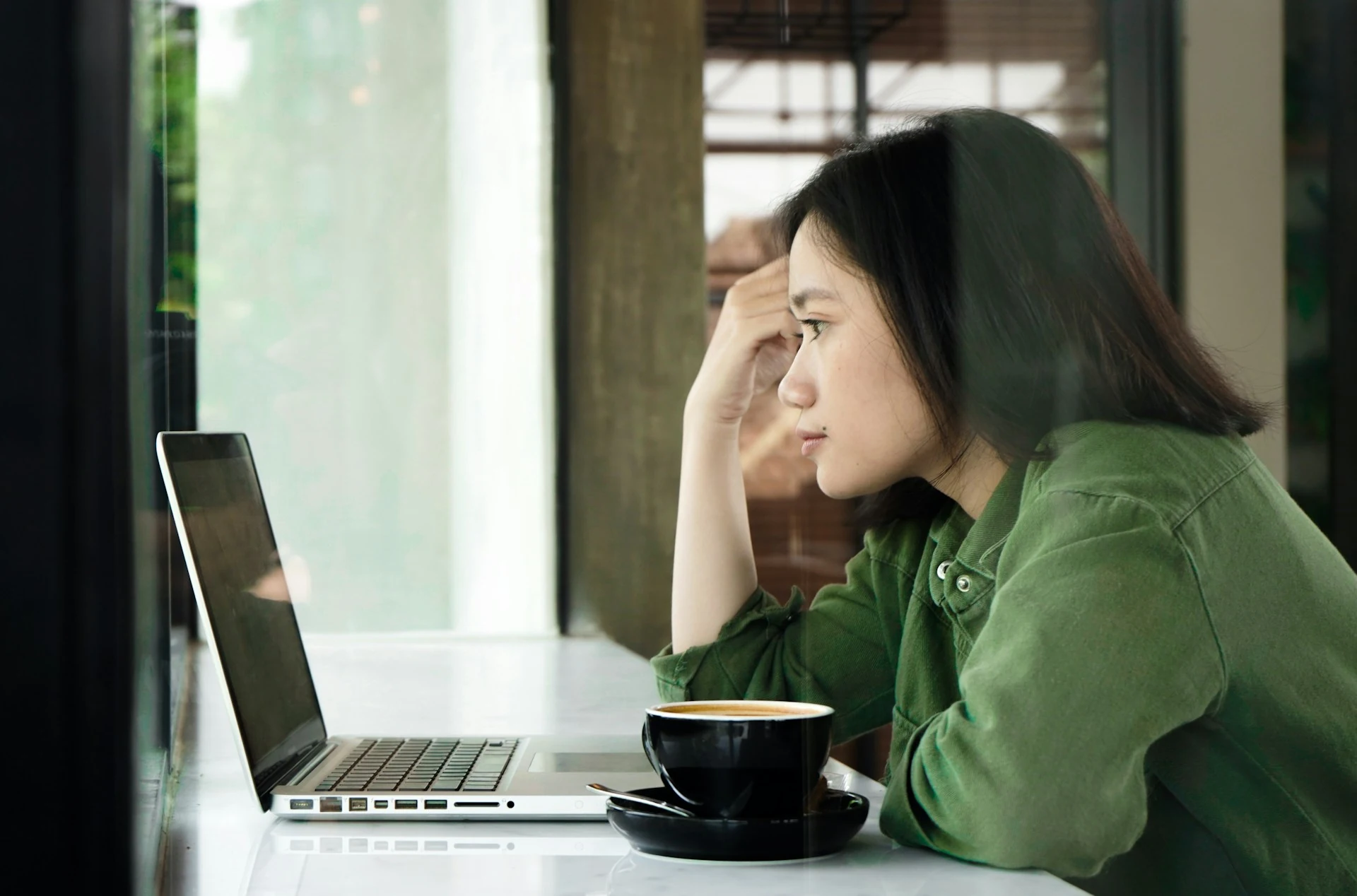 A woman in a green jacket looking at her laptop.