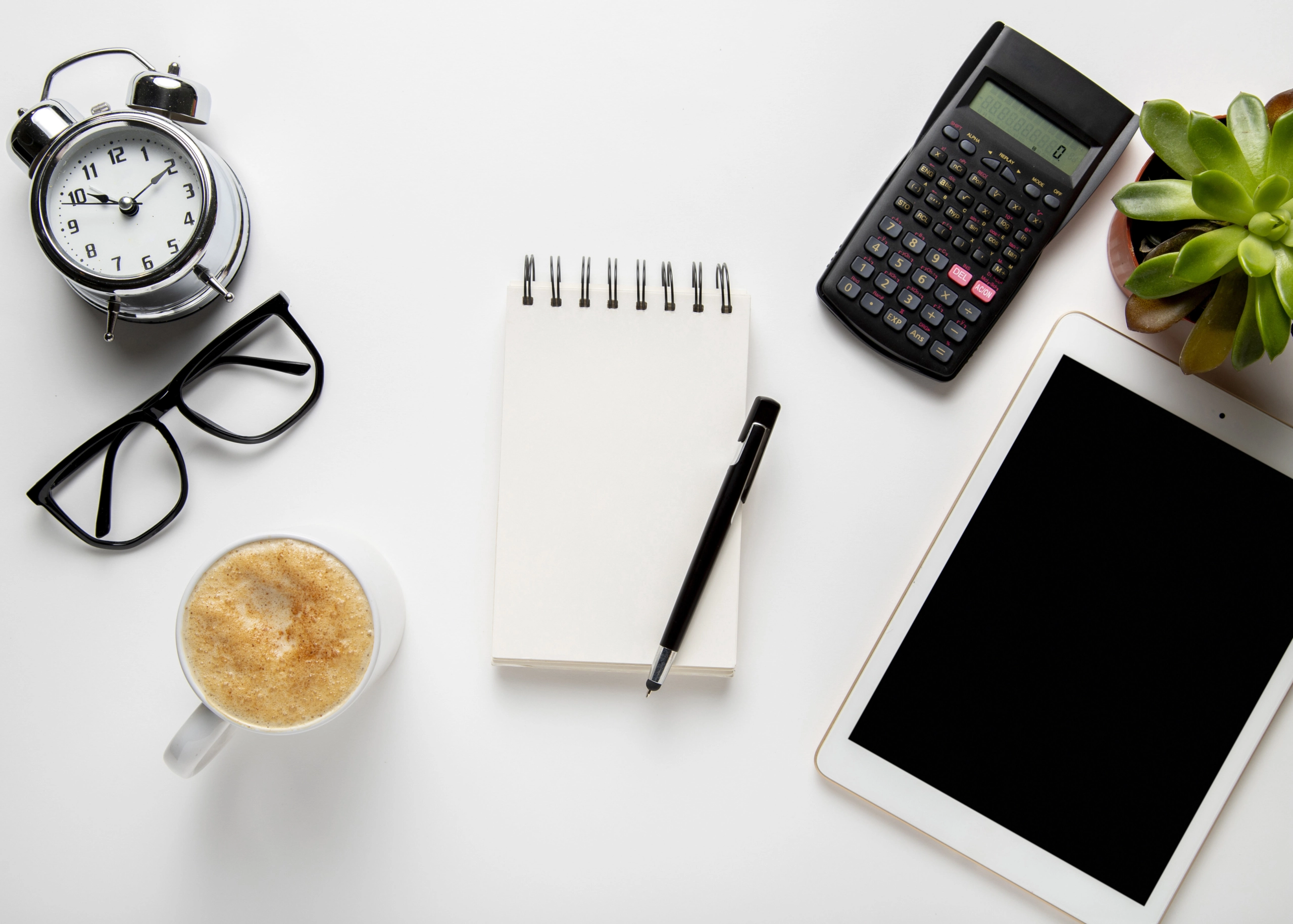 Desk setup with alarm clock, calculator, notepad, and tablet representing work time tracking and hour calculations.